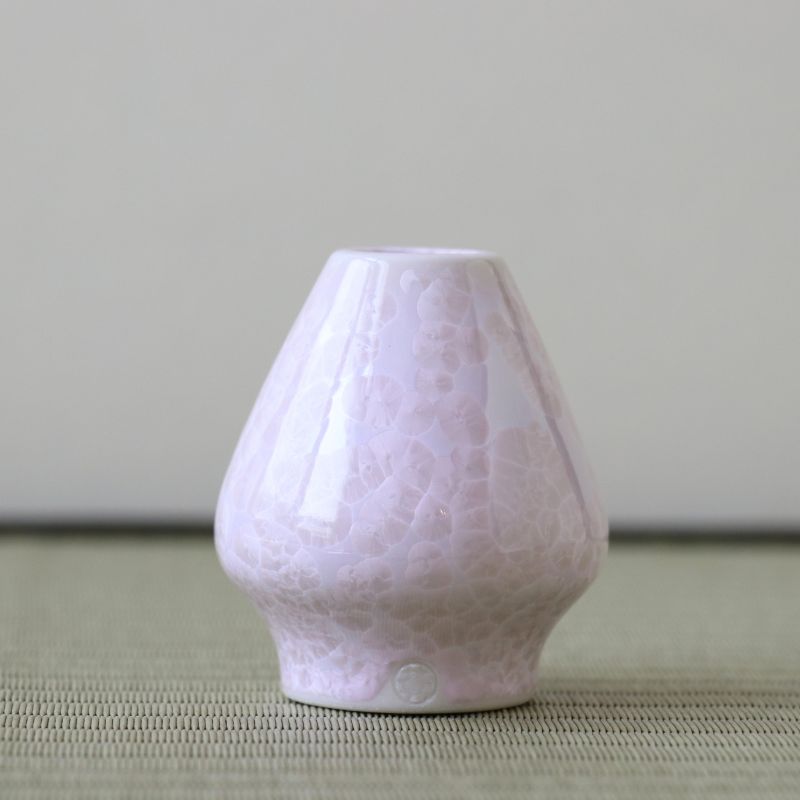 Matcha whisk stand holder on a light green surface with a neutral background