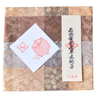 Decorative box with a white card featuring a red illustration of yarn and text on a patterned background.