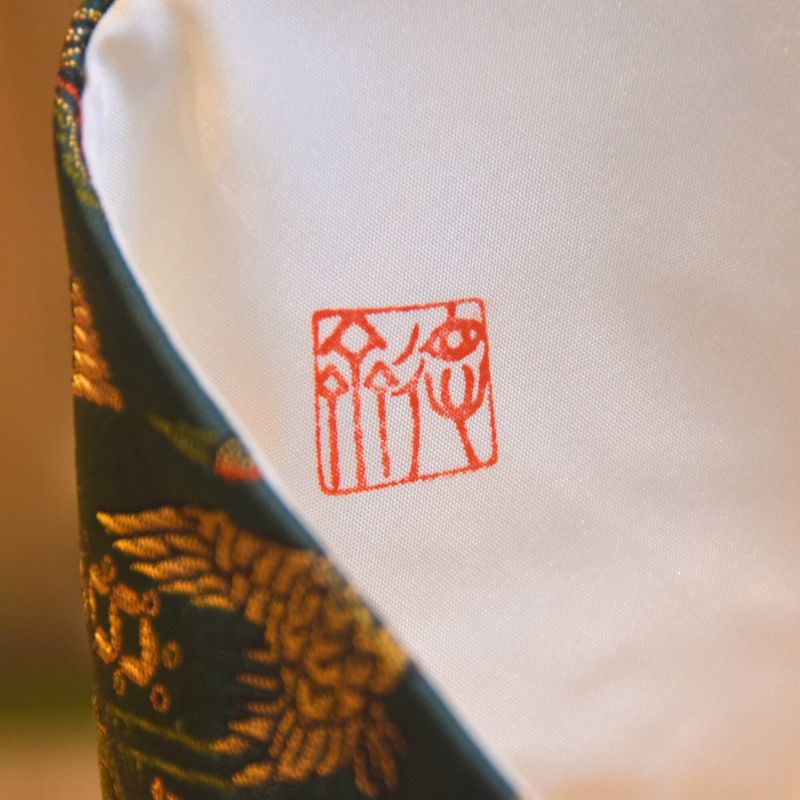 Close-up of a fabric with a red logo and green pattern on a white background
