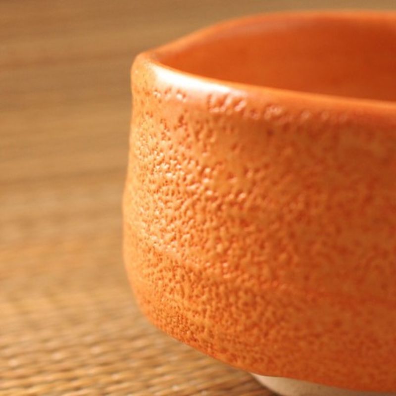 Enlarged photo of Nara Tea Co.'s Akashino Matcha Tea Bowl with a slightly rough texture and an elegant orange color, viewed from the front from the side.