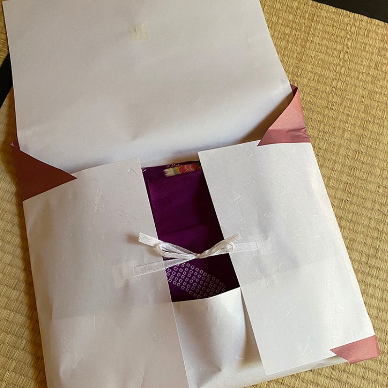 Nara Tea Co. 10-piece set of Tatoushi l kimono Storage Paper with Strings, one of the packages was opened to reveal a purple kimono with knots in the interior and a knot in the string.
