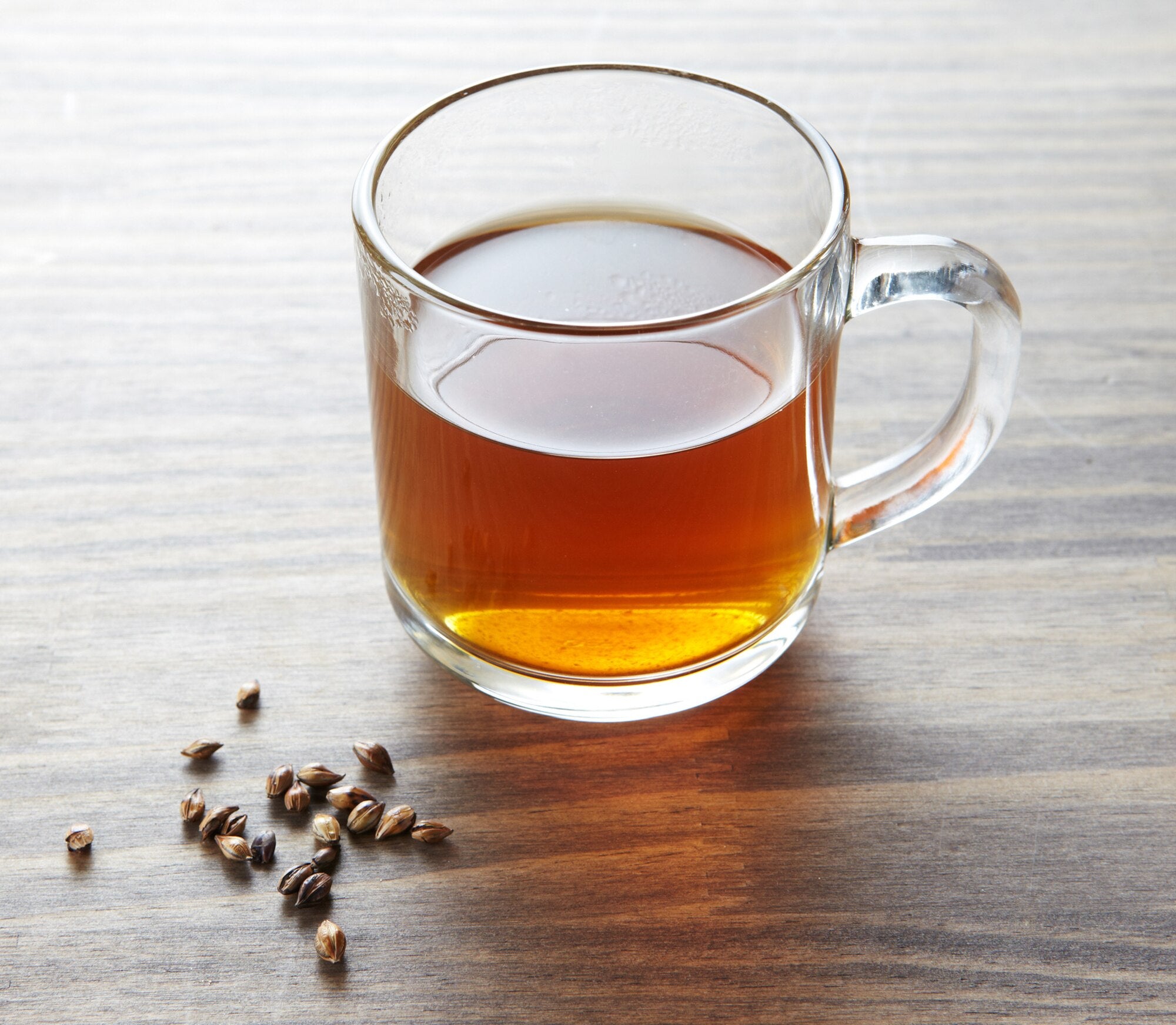 Clear glass mug with tea on a wooden surface with scattered coffee beans.