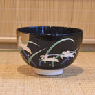 Black ceramic bowl with white rabbit and grass design on a woven mat background