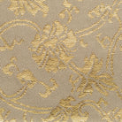 A close-up of a woven fabric with an ornate floral damask pattern in metallic gold over a warm beige background.