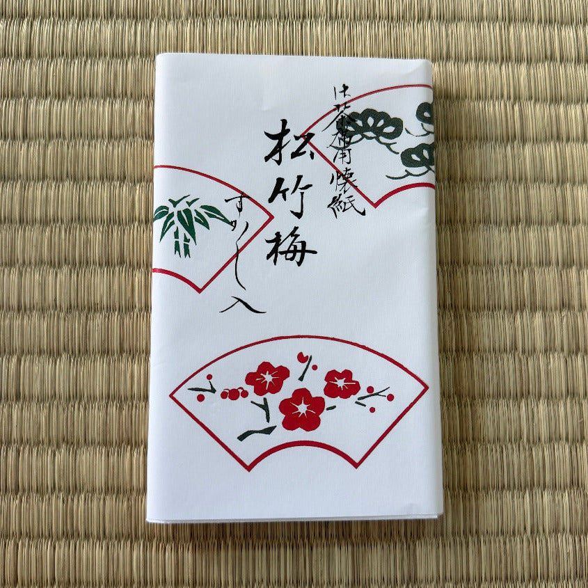 White box with red floral designs and black text on a woven mat background