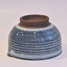 Ceramic bowl with blue glaze and brown rim on a white background