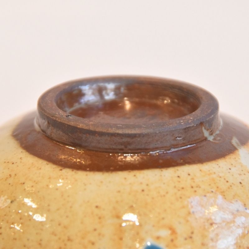 Close-up of a ceramic jar with a brown glaze on a beige background