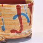 Ceramic pot with red and blue abstract designs on a white background