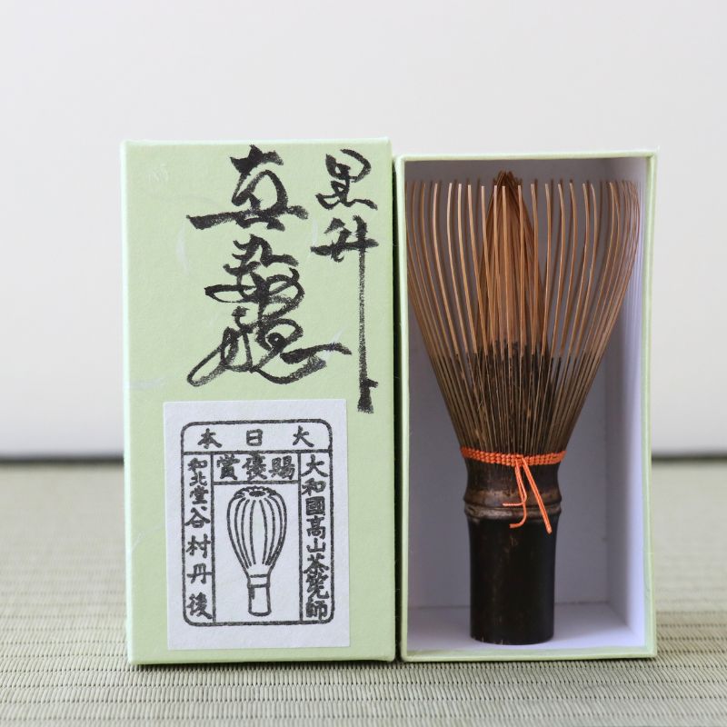 Bamboo whisk with wooden handle and green box on a light background