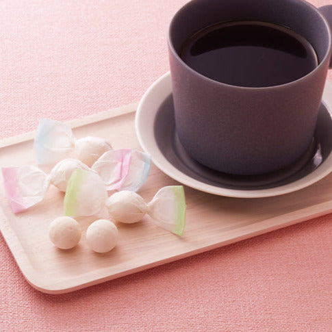 Cup of coffee on a saucer with pastel wasanbon sweets candies on a pink background