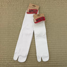 A pair of white tabi-style split-toe socks with brown paper hanger tags reading 'NINJA SOCKS,' laid flat on a textured beige woven mat.