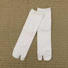 A pair of white tabi socks laid flat on a textured beige woven mat background.