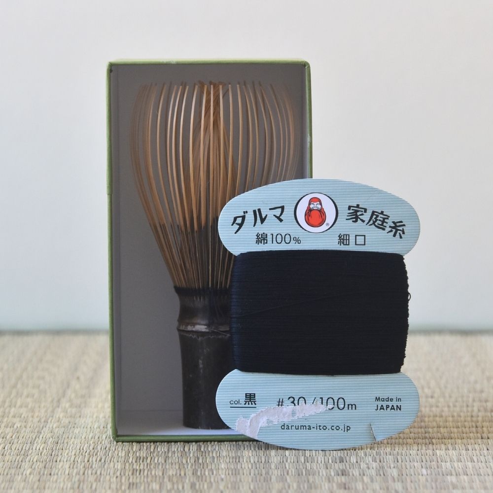 Matcha whisk and green tea strings with Daruma Ito branding on a textured surface.