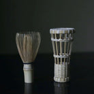 Two woven tea-making tools on a dark surface with a dark background