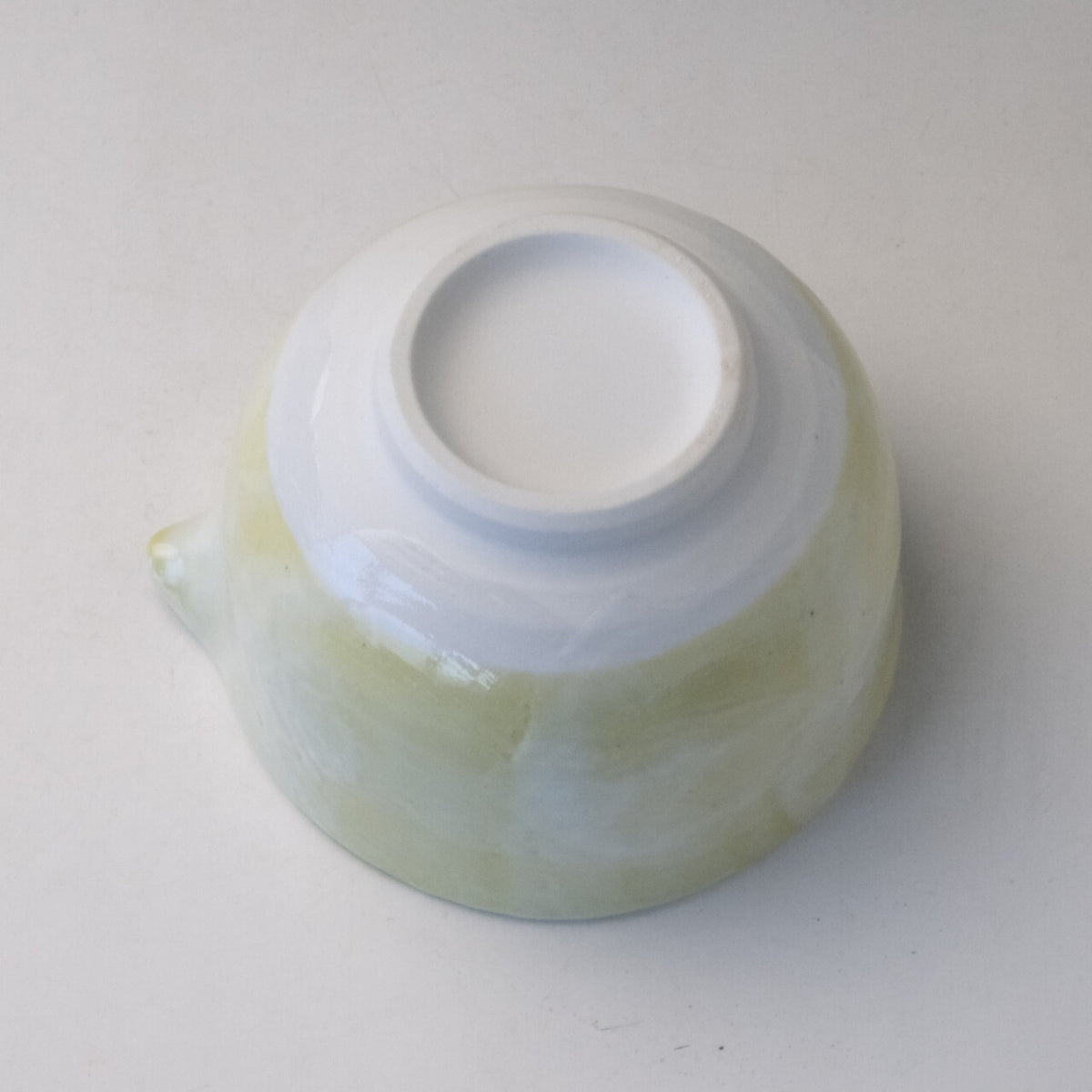 Underside view of the pale yellow Mino Ware katakuchi matcha bowl showing its white ceramic foot and cloudy glaze