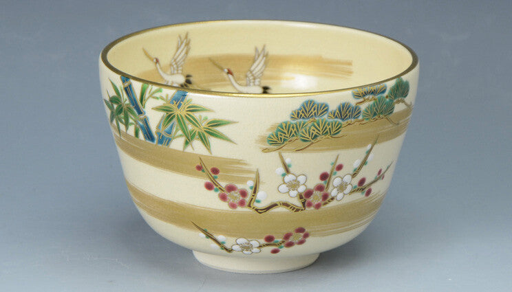 Angled view of the Kyo Ware matcha bowl showing cranes, pine, bamboo and plum decoration with gold leaf accents