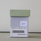 A small light green and white product box with a barcode label and handwritten price sticker, photographed against a plain light background.