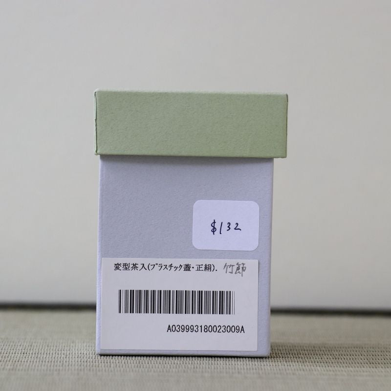 A small light green and white product box with a barcode label and handwritten price sticker, photographed against a plain light background.