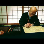 Man writing on paper with a brush in a traditional setting