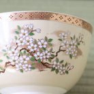 Close-up of the Eika Miyaji matcha bowl showing hand-painted cherry blossoms, green leaves, and intricate gold detailing