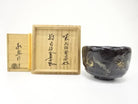 Pre-owned Eiko Meido Mandokoro Kiln matcha bowl with a midnight glaze and gold botanical accents displayed beside its inscribed wooden storage box.