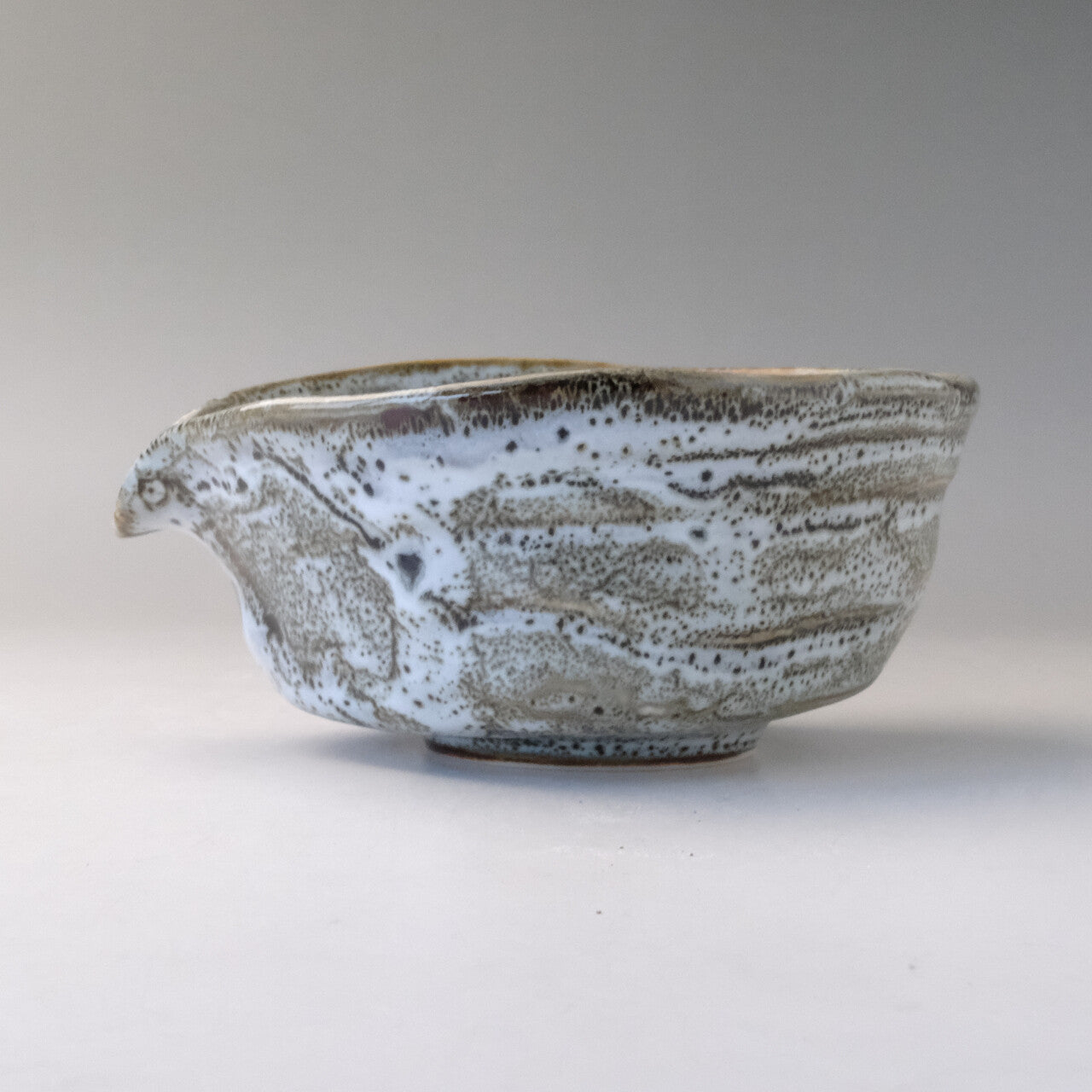 Left-side profile of the katakuchi matcha bowl showing the low foot, pouring spout, and flowing gray and white glaze markings.
