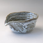 Three-quarter view of a gray and white Mino Ware katakuchi matcha bowl with a pointed pouring spout, layered glaze, and textured ridges.