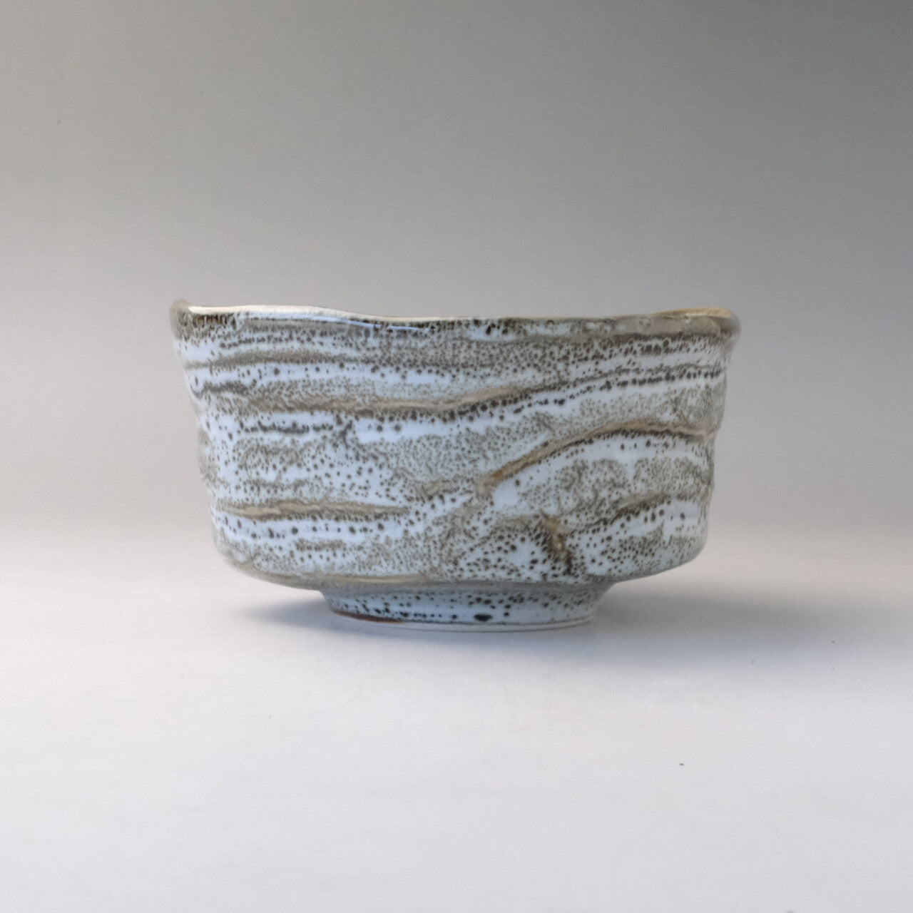 Rear profile of the Mino Ware matcha bowl showing its low rounded form, horizontal ridges, and snow-washed gray and white glaze.