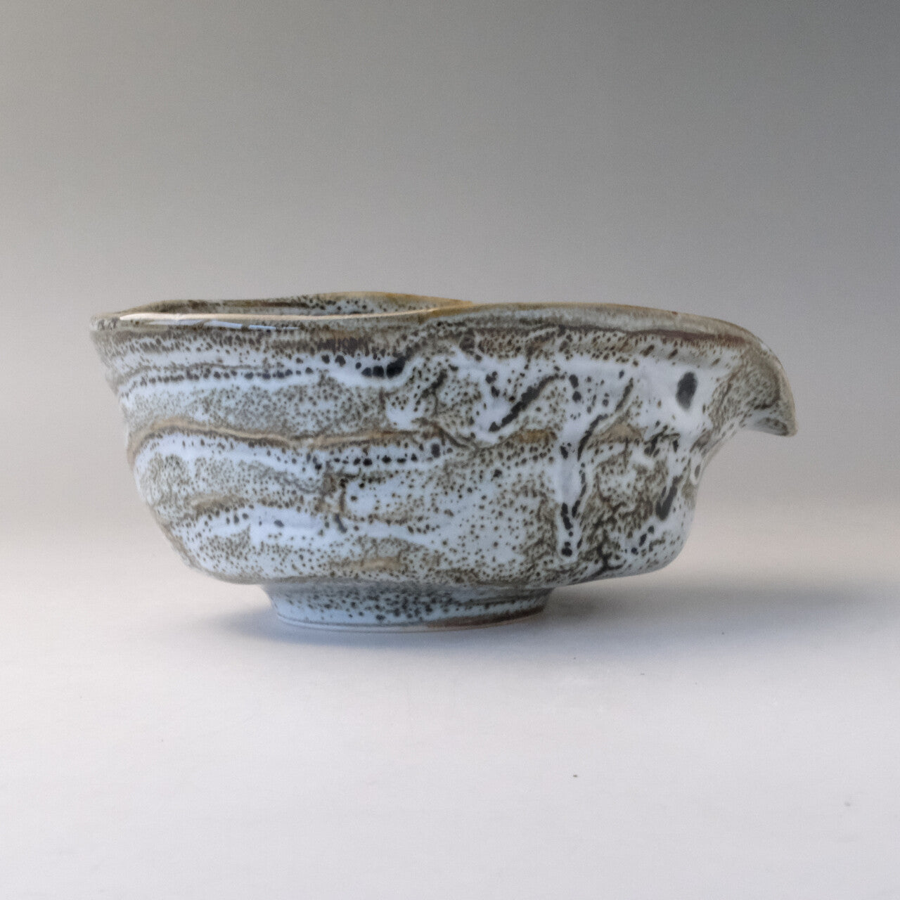 Right-side profile of the gray and white katakuchi bowl showing the projecting spout and irregular layered glaze.
