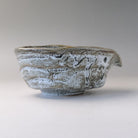 Right-side profile of the gray and white katakuchi bowl showing the projecting spout and irregular layered glaze.