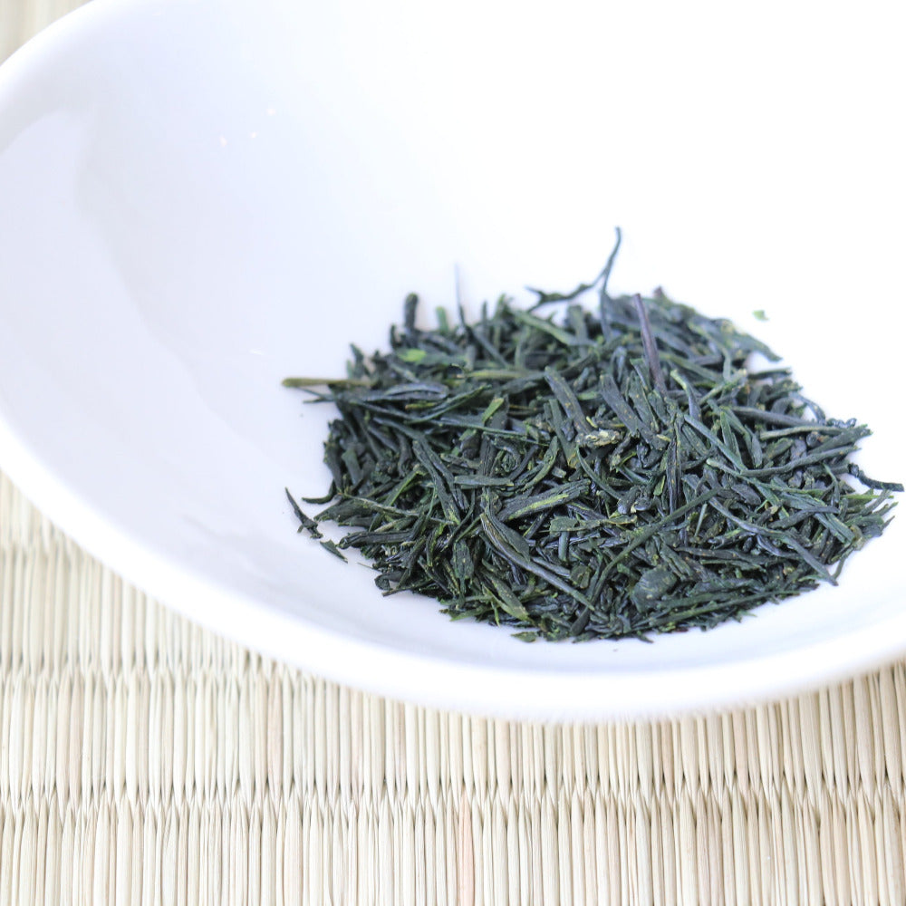 White bowl with green tea leaves on a woven mat