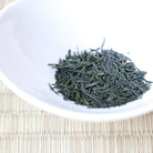 White bowl with green tea leaves on a woven mat