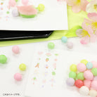 Pastel-colored round candies with a smartphone and floral decorations on a white surface.