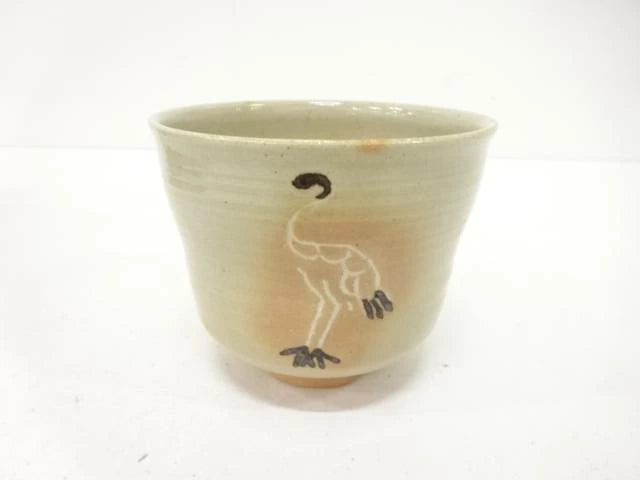 Front view of the Hiroshi Fukumori chawan showing a graceful standing crane against a warm ivory glaze with subtle ochre tones near the foot.