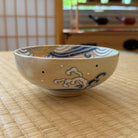 Front view of a hand-painted Kyo Ware matcha bowl with cobalt-blue curling waves, white foam, and ochre-gold accents on a cream glaze.