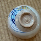 Underside view of the hand-painted matcha bowl showing its circular foot ring and cobalt-blue wave decoration around the lower exterior.