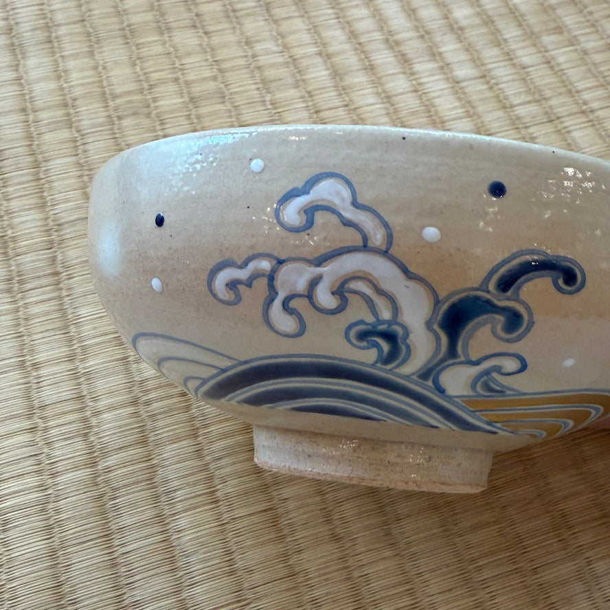 Angled exterior view of the Kyo Ware matcha bowl showing a large cresting wave with curling blue lines and white foam.