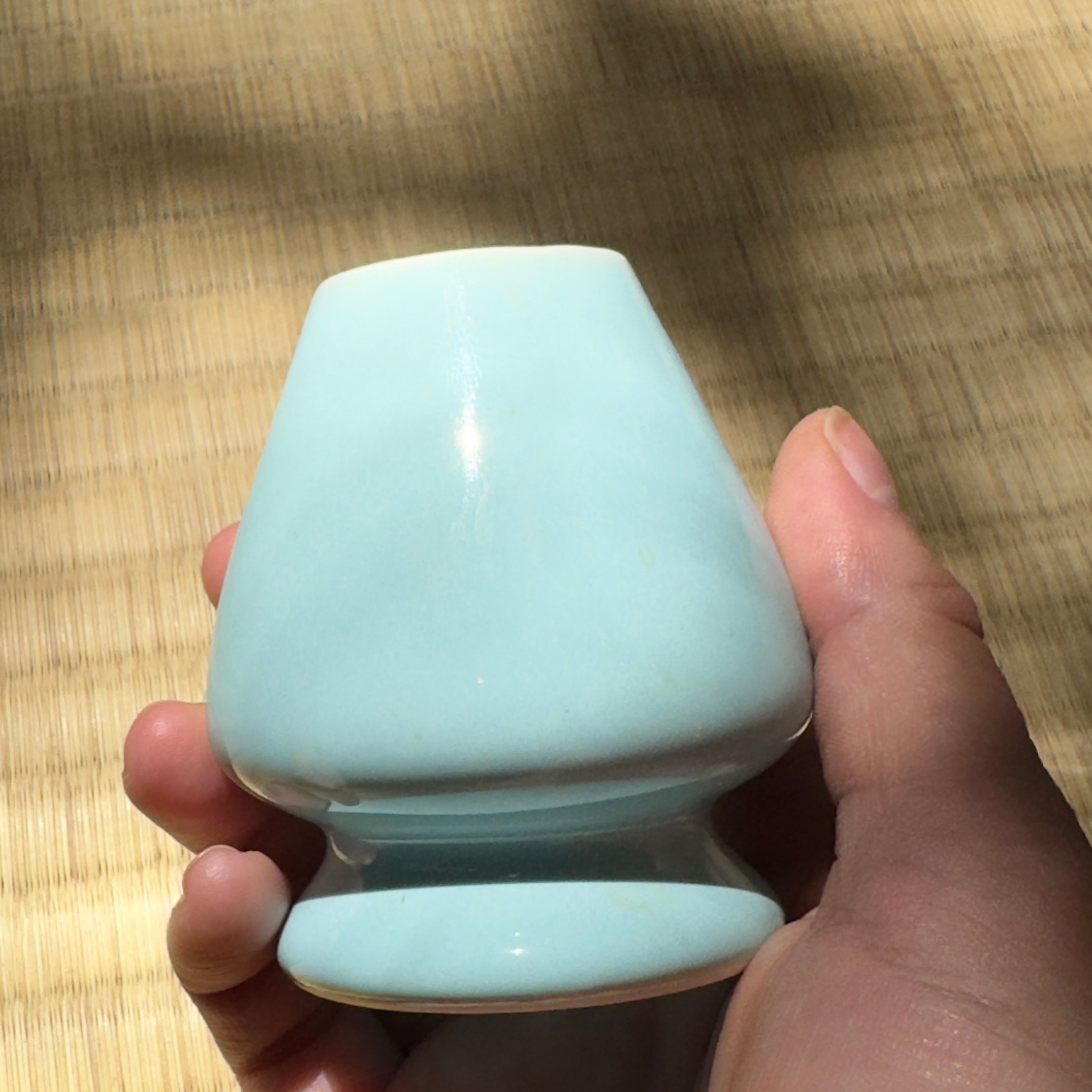 Light blue ceramic whisk stand held in a hand 