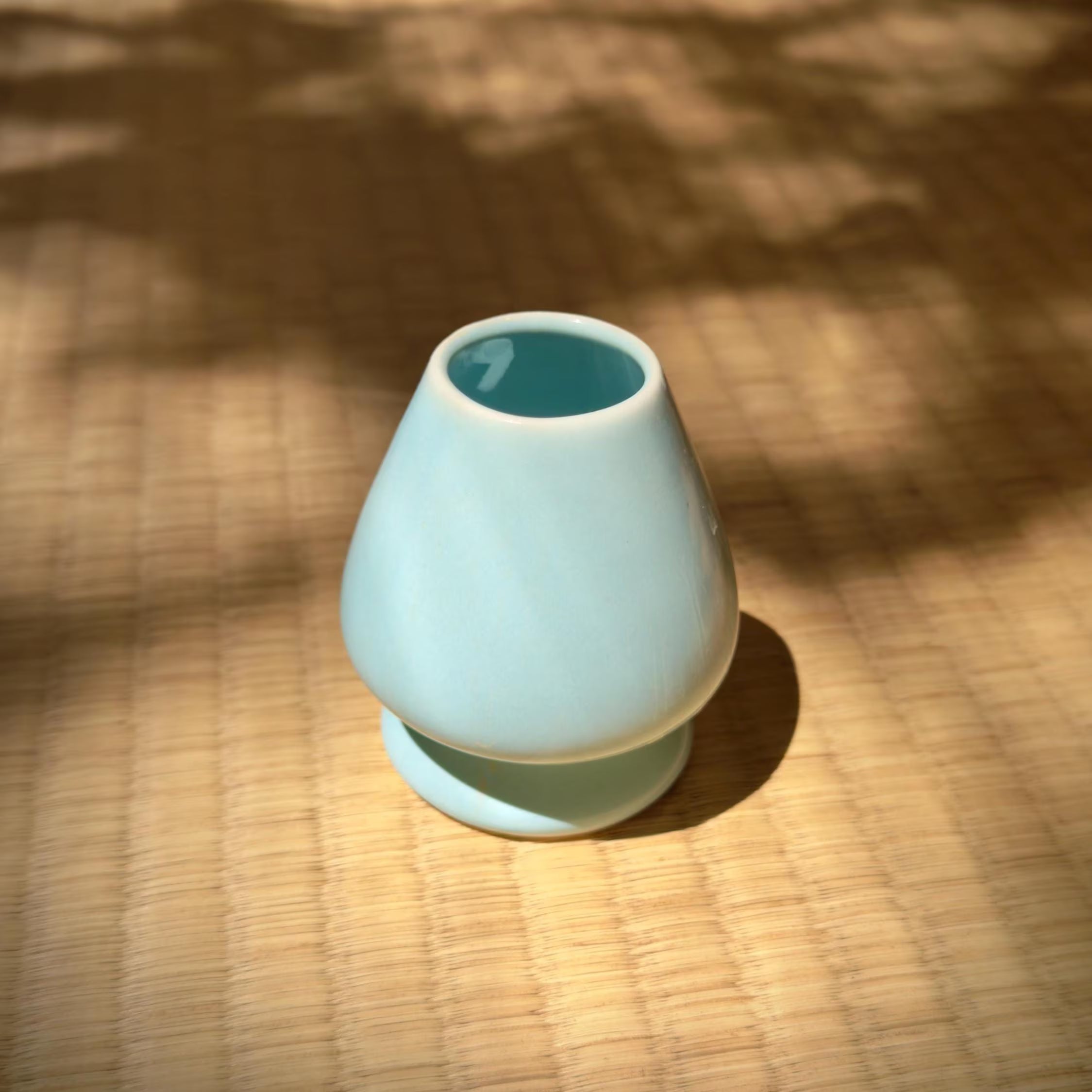 Blue ceramic whisk holder with a blue interior on a tatami mat textured surface