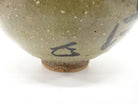 Close-up of the lower exterior showing a small dark painted mark, pale speckled glaze, and warm exposed clay around the foot.