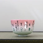 Side view of the Kagetsu Kiln Rikyu Shichisoku matcha bowl showing Japanese calligraphy across the pink and pale green glazed exterior