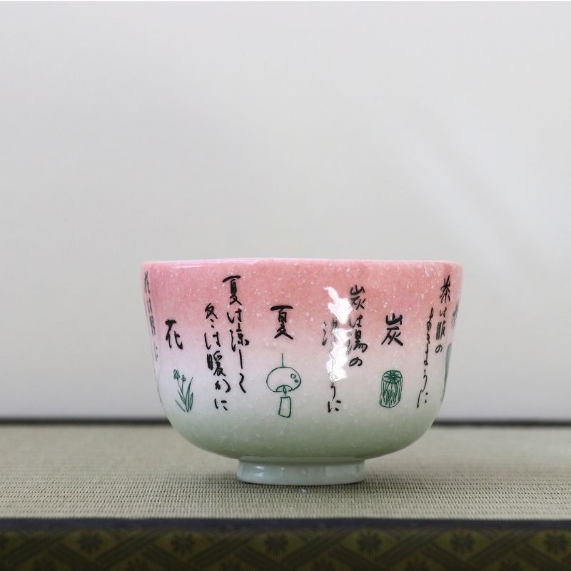 Side view of the Kagetsu Kiln Rikyu Shichisoku matcha bowl showing Japanese calligraphy across the pink and pale green glazed exterior
