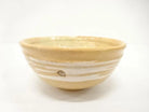 Front view of the Kahei Shima Raku chawan showing its softly irregular rim and layered sand, cream, and ivory glaze.