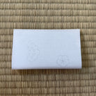 White rectangular object with embossed designs on a woven mat background