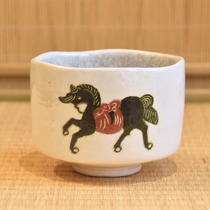 Front view of the white Raku matcha bowl showing the running black horse motif and softly irregular cylindrical form.