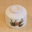 Underside angle of the Shiro Raku matcha bowl showing its pale raised foot and painted horse motif wrapping around the cream-white exterior.