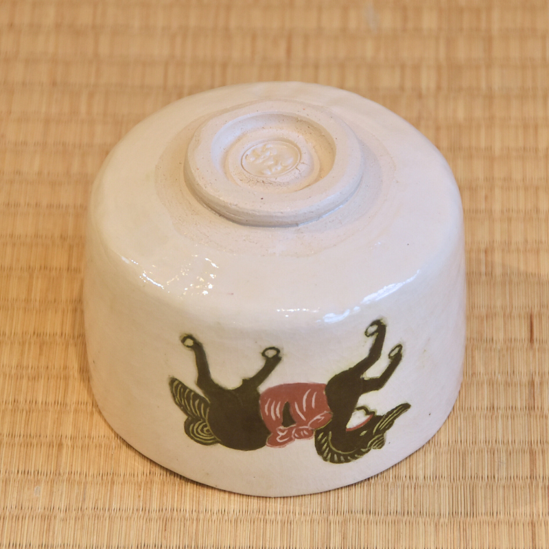 Underside angle of the Shiro Raku matcha bowl showing its pale raised foot and painted horse motif wrapping around the cream-white exterior.