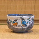 Front view of a hand-painted Kutani Ware matcha bowl decorated with two colorful kingfishers, a fish, and leafy branches above a blue-gray glaze.