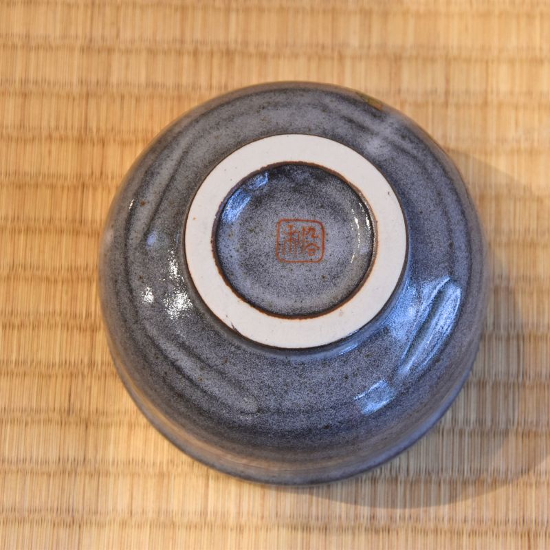 Underside view of the blue-gray Kutani Ware matcha bowl showing its pale foot ring and red artist mark.