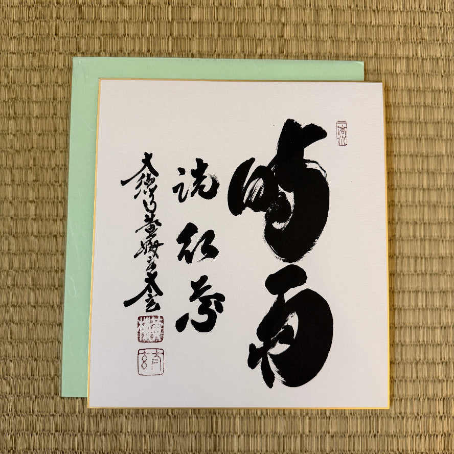 Card with black calligraphy on a white background, placed on a woven mat.